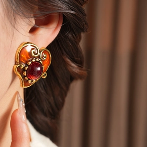 Close-up of vintage heart earring with red resin and gold filigree on model's ear