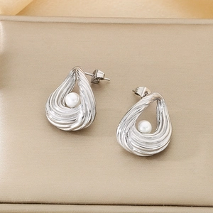 Close-up of silver steel oval earrings with wavy texture and centered white pearl
