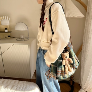 Detailed close-up of a large green plaid tote bag with a cute brown bear plush pendant