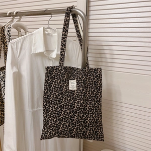 Detail of leopard print canvas tote bag hanging on a silver hanger with white woven label