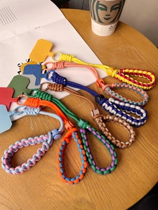 Multiple colors of woven phone wrist straps with pads displayed on a wooden table