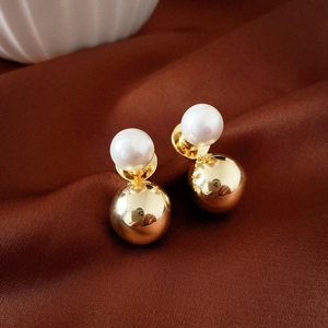 Detail of two-sided gold ball and white faux pearl earrings on brown silk background