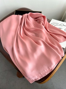 Detail shot of a soft pink satin scarf draped elegantly on a textured leather chair