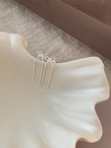 Detail of silver bow earrings with long tassel chains on a white ceramic tray