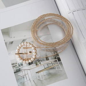 Detail of transparent PVC belt featuring gold bead edges and a round pearl buckle on a magazine
