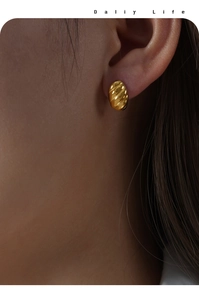 Close-up of a gold C-shaped earring with textured twist design worn by a model