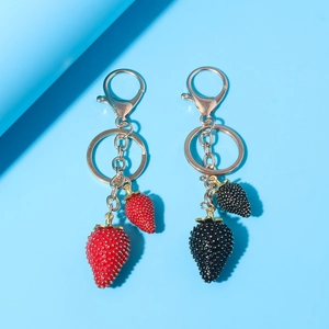 Close-up of red and black strawberry keychains with gold hardware on blue background
