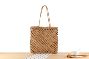 Close-up of beige hollow handmade woven straw tote bag on a wooden table with decor