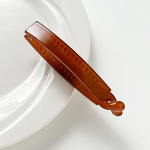 Minimalist brown plastic banana hair clip with a stylish twisted knot on a white surface
