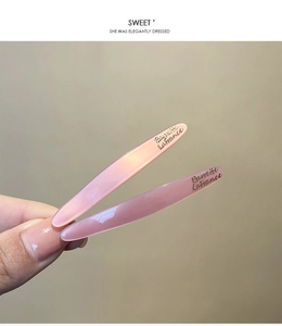 Detail of two pink translucent resin barrettes with French lettering held in hand