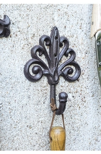Detailed texture of rustic brown cast iron wall hook with floral lily pattern on stone wall