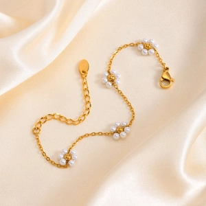 Detailed macro shot of 18K gold bracelet with pearl flowers on champagne silk