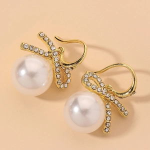 Close-up of elegant bow design with sparkling zircons and white pearls on gold earrings