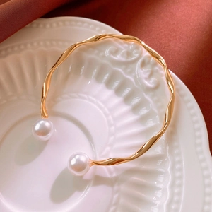 Detailed view of a gold wavy cuff bracelet with white pearls on a ceramic plate