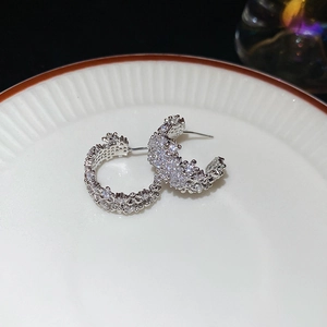 Macro shot of silver C-shaped earrings with shimmering cubic zirconia on ceramic plate