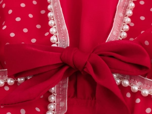 Dettaglio vestito rosso a pois con pizzo bianco, perle e un grande fiocco rosso elegante