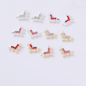 Flat lay of bow-shaped nail charms with gold plating, pearls, and sparkling rhinestones