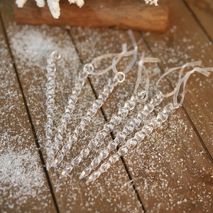 Set of six clear acrylic spiral icicle ornaments on snow-covered dark wood background
