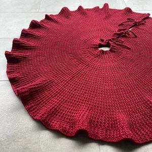 Macro view of deep red knitted Christmas tree skirt with ruffled edges and tie closure