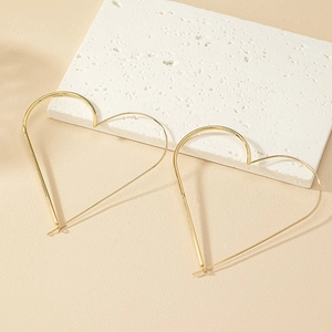 Detail of large minimalist golden heart-shaped earrings on a textured stone board