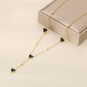 Detail view of a gold titanium necklace featuring black hearts and zircon charms on a display box