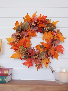 Close-up of autumn wreath with maple leaves and berries on white wooden wall background