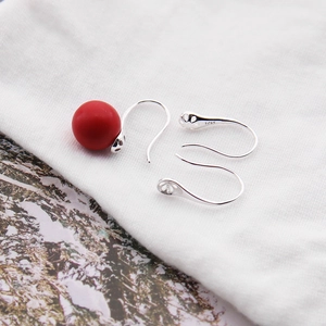 Macro shot of S925 sterling silver ear hook with a red matte bead on a textured background