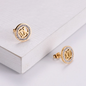 Golden round earrings with Roman numerals and sparkling crystals on white stone surface