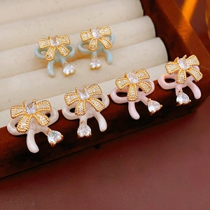 Close-up of bow earrings with blue, white, and pink enamel and heart-shaped zircons