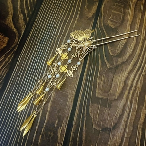 Golden butterfly hair pin with cascading tassels and pearls on a dark wood background