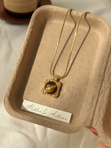 Macro shot of vintage gold tiger eye pendant on snake chain in a rustic tray