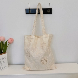 Detailed close-up of 3D floral embroidery and lace cutouts on the cream canvas tote bag
