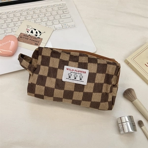 Detailed corduroy makeup bag with brown checkerboard pattern and side handle on desk