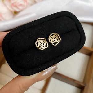 Detailed view of hollow rose flower earrings in gold finish on black velvet display