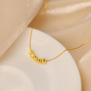 Macro shot of gold necklace featuring six textured beads on a white plate with satin backdrop