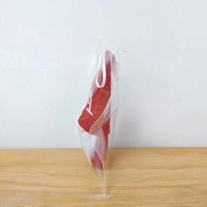 Close-up of a red knitted Christmas gnome ornament in clear packaging on a wooden surface
