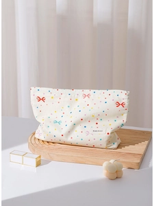 Cream bow cotton makeup bag with colorful polka dots on a wooden tray with accessories