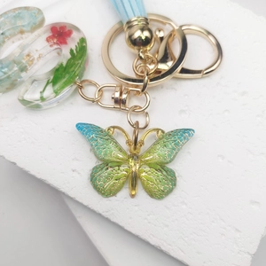 Detail of green butterfly keychain with dried flower resin letter S and blue tassel