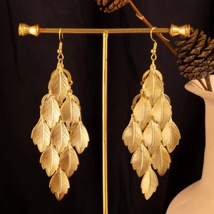 Macro shot of gold layered leaf drop earrings hanging on a display stand with pine cone