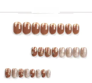 Close-up of caramel brown press-on nails with golden floral patterns and rhinestones