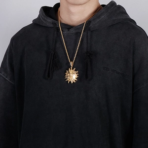 Detailed view of a gold sun face pendant on a twist chain worn over black clothing