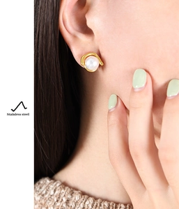 Detailed close-up of a stainless steel gold earring with a white pearl on a female model