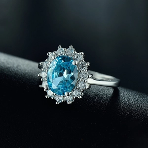 Vintage sterling silver ring with oval blue gemstone and zircon halo on black leather background