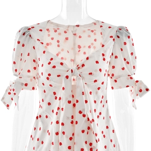 Détail d'une robe blanche à manches bouffantes avec imprimé cerises et nœuds décoratifs