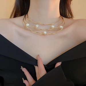 Detail of gold layered wavy necklace with baroque pearls on model collarbone