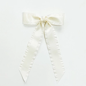 Detailed view of cream bow hair clip featuring delicate ruffled edges and long satin ribbons