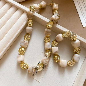 Close-up of cream marble resin beads and irregular gold metal charms on the jewelry set