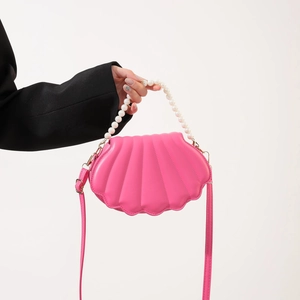Close-up of pink shell-shaped bag featuring a pearl handle and textured finish