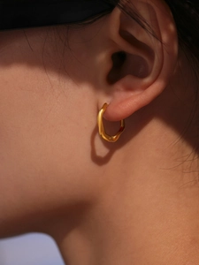 Détail macro des boucles d'oreilles dorées en acier inoxydable à texture ondulée