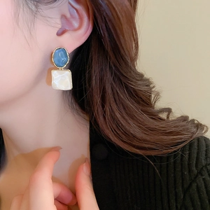Close-up of geometric earrings with blue oval stones and white marble square drops
